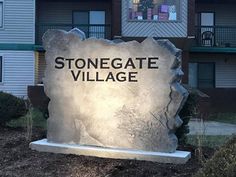 a stone sign that says stonegate village in front of a building with balconies