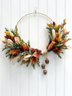 a wreath with dried flowers and bells hanging on a white painted wall in front of a door