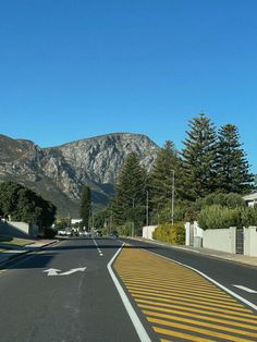 an empty street with mountains in the background and yellow lines painted on the road to indicate that there is no traffic