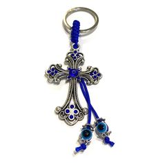 a blue key chain with an ornate cross and two evil eye charms on it's end