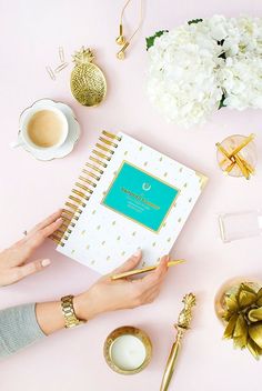 a person holding a notebook on top of a pink table next to flowers and candles