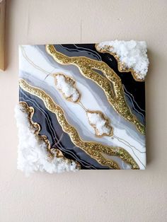 an abstract painting on the wall with gold and black paint, surrounded by white pom poms