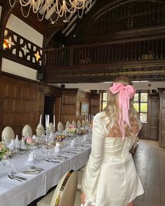 a woman standing in front of a long table with white clothed tables and chandeliers