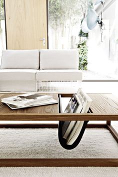 a coffee table with magazines on it in front of a white couch and large window