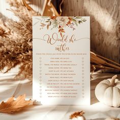 a white card with gold lettering on it next to some autumn leaves and pumpkins