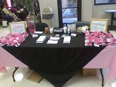 a black table with pink flowers and cards on it in front of two people sitting at tables