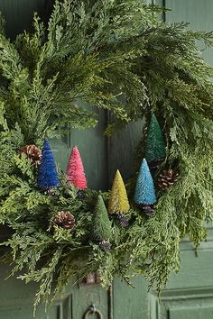 a christmas wreath with pine cones and evergreen needles hanging from the side of a green door