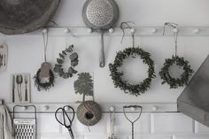 kitchen utensils are hanging on the wall with wreaths and potted plants