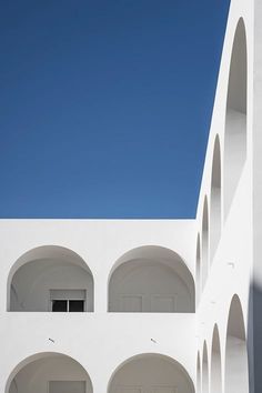 an empty white building with arches on the outside and blue sky in the back ground