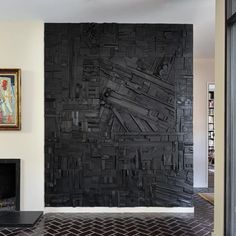 a large black piece of art hanging on the side of a wall next to a fireplace