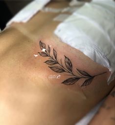 a tattoo on the back of a woman's stomach that is covered in leaves