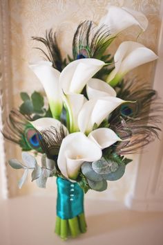 a vase filled with white flowers and peacock feathers on top of a table next to a window