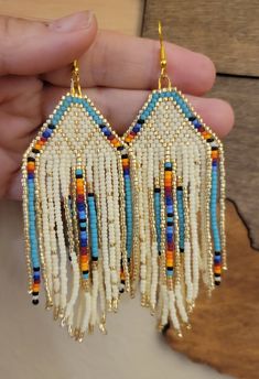 a pair of white and blue beaded earrings with fringes hanging from it's sides