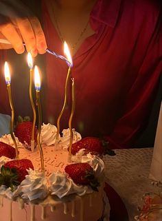 a person lighting candles on a cake with strawberries