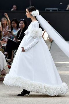 a woman in a white wedding dress and veil walking down the runway at a fashion show