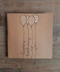 a brown card with three balloons attached to the front of it on a wooden surface