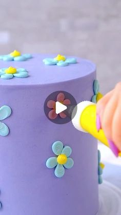 someone is decorating a purple cake with blue and yellow flowers on the frosting