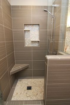 a walk in shower sitting next to a tiled bathroom wall with a bench on the side