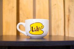 a white coffee cup with the word lake on it sitting on a black table next to a wooden wall