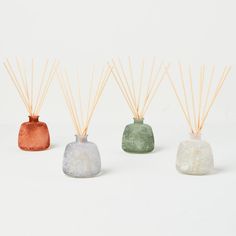 three different colored candles with sticks sticking out of them on a white surface, one in the shape of a bell