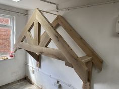 an unfinished wooden bed frame hanging from the ceiling in a room with white walls and exposed pipes