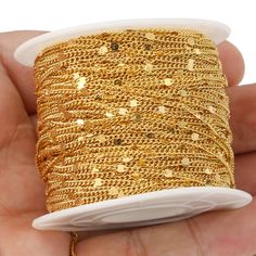 a hand holding a spool of gold colored thread