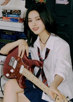 a young woman sitting on the floor with a guitar in her lap and wearing a tie