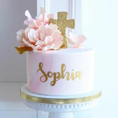 a pink cake with gold lettering and flowers on top is sitting in front of a white door