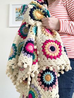 a woman is holding a crocheted blanket in her hands