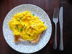 a white plate topped with scrambled eggs next to a fork and knife on top of a wooden table