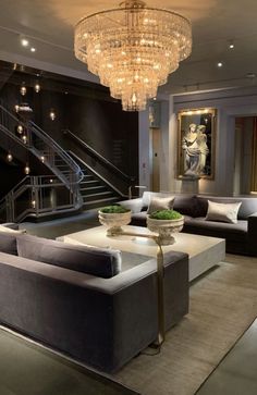 a living room with couches and a chandelier hanging from the ceiling in front of a staircase