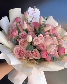 a bouquet of pink roses and white tulips is being held by someone's hand