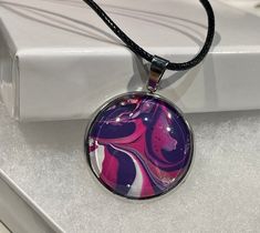 a glass pendant with a pink and purple swirl design on it sitting on top of a white box