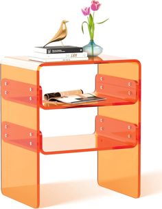 an orange shelf with some books and a vase on top of it next to a flower