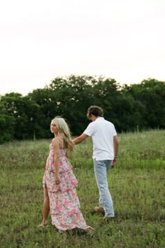 a man and woman standing in a field holding hands