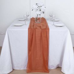 the table is set with white and orange linens, wine glasses, and flowers