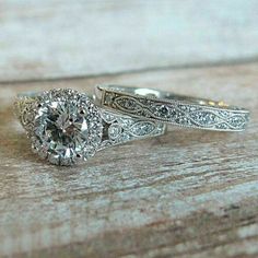 two engagement rings with an old - fashioned design on the side, sitting on top of a wooden surface