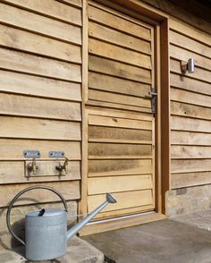 a watering can sitting in front of a wooden building with an open door and handle