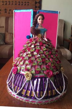 a barbie doll in a dress made out of candy wrappers and flowers on top of a table