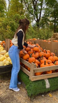 a woman standing next to a pile of pumpkins in a wooden crate on top of grass