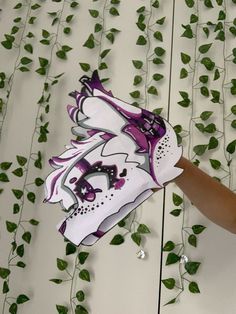 a person holding up a paper mask with vines growing on the wall behind it and in front of them