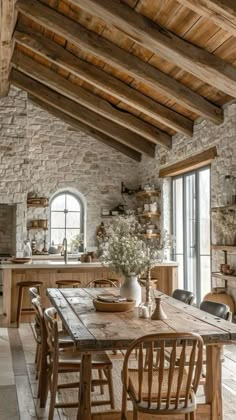 a rustic dining room with stone walls and exposed beams, wooden table surrounded by chairs