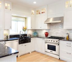 a kitchen with white cabinets, black counter tops and stainless steel stove top oven in the center