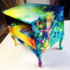 a multicolored painted dresser sitting on top of a white table