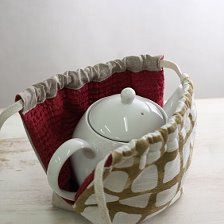 a tea pot in a basket with a red and white cover on the inside, sitting on a table