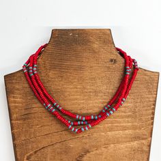 Three strand beaded choker necklace with red  and turquoise beads. The necklace is taken on a  brown block and a white background. Red Wooden Beaded Necklaces, Red Wooden Beaded Necklace, Red Wooden Beads For Festivals, Red Bohemian Necklace With Heishi Beads, Red Necklaces With Wooden Beads For Festival, Red Tiny Beaded Necklaces For Festival, Red Adjustable Beaded Necklaces With Spacer Beads, Red Beaded Necklaces For Festival, Adjustable Red Necklace With Colorful Beads