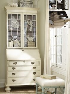 a white china cabinet sitting in front of a window next to a footstool