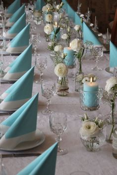 the table is set with white flowers and blue napkins, candles and place settings