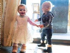 two toddlers standing next to each other in front of a window and holding hands