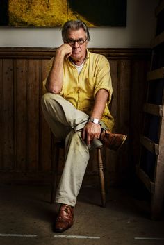 an older man sitting in a chair with his hand on his chin and looking at the camera